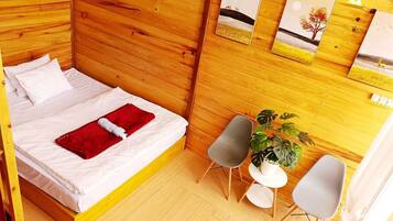Una habitación de madera con una cama, dos sillas, una mesita y una planta en maceta.