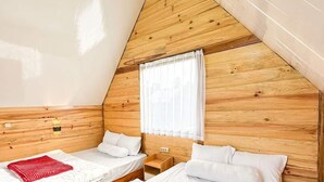 Una habitació amb dos llits, parets de fusta, una finestra amb cortines blanques i un sostre inclinat.