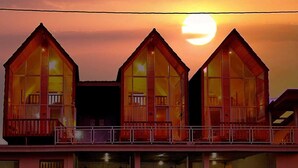 Una fila de tres cabanes de fusta amb grans finestres, un balcó i una barana.