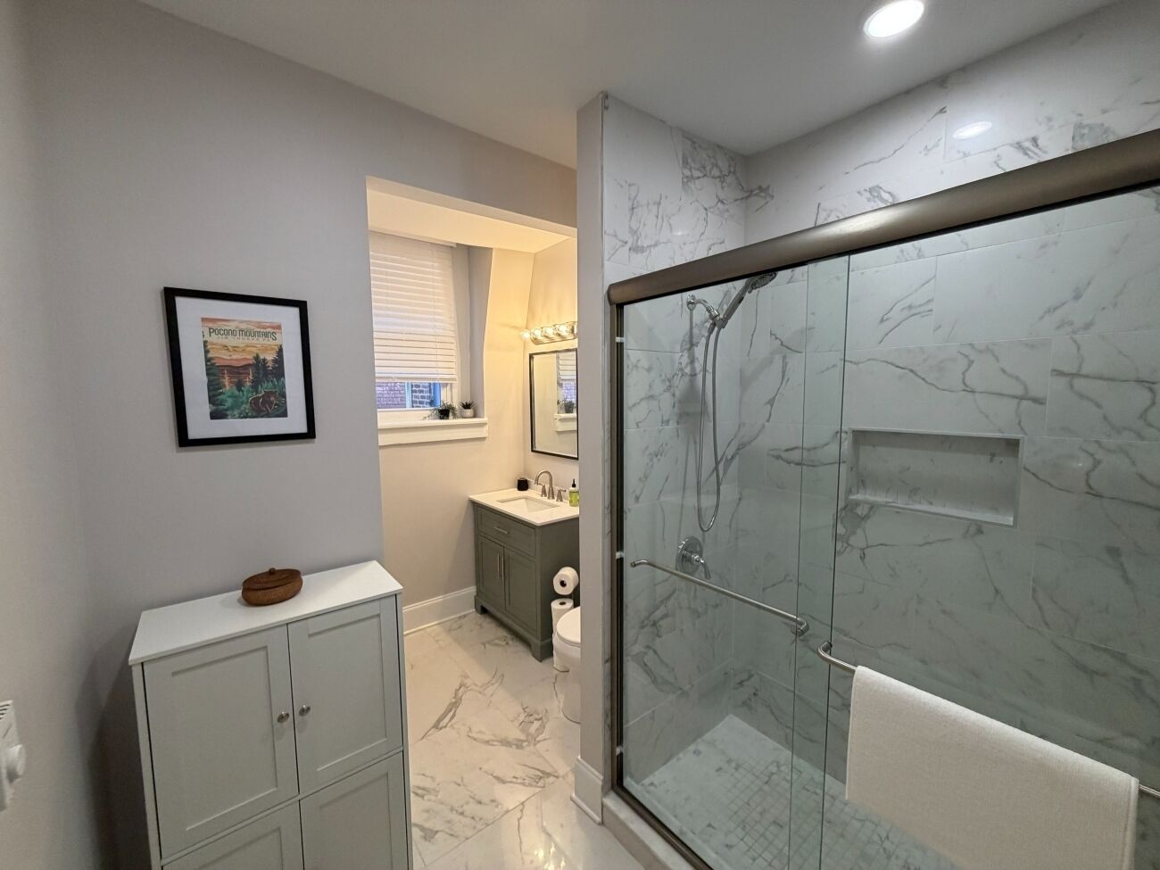 A bathroom with a marble shower, a sink, and a cabinet.