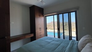 Un dormitori amb un llit, un ventilador de sostre, un armari de fusta i vistes a una piscina i al paisatge.