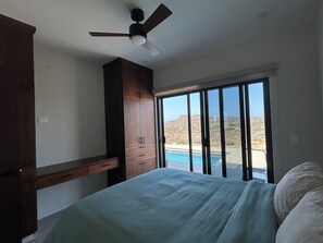Une chambre à coucher avec un lit, un ventilateur de plafond, une armoire en bois et une vue sur une piscine et un paysage.