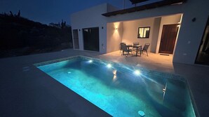 Una piscina rectangular amb un videt de rajola, envoltada per un patio amb una taula i cadires.