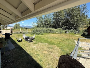 A covered patio area with a grill, outdoor seating, and a view of a grassy yard with trees and a fence.