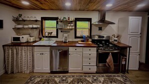 A kitchen with wooden ceiling, white cabinets, a stove, a dishwasher, and a window with a view of greenery.