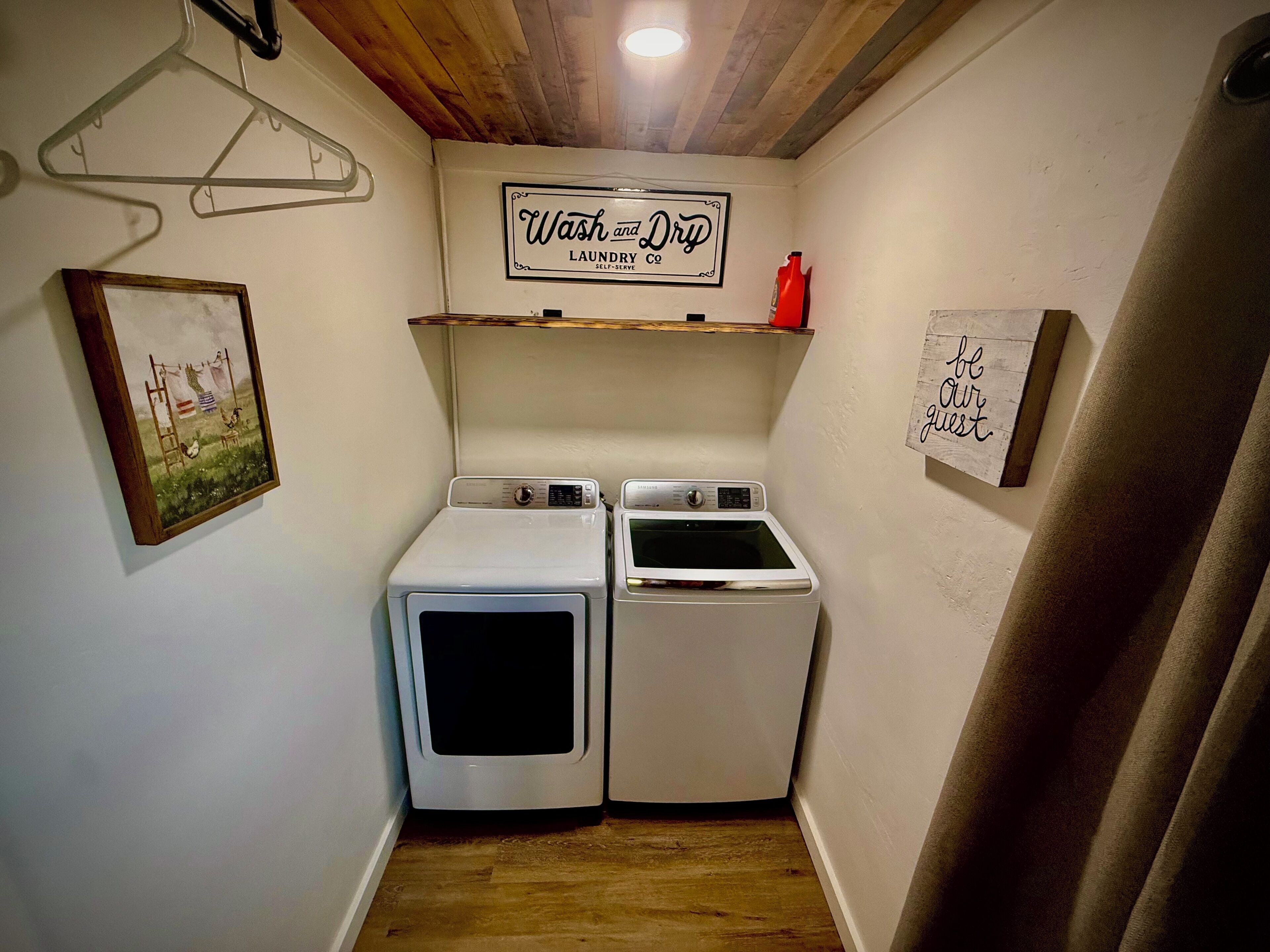 Een wasruimte met twee witte wasmachines en drogers, een bord met daarop 'Wash and Dry', een afbeelding van een wasscene, en een bordje met 'Your Guest'.