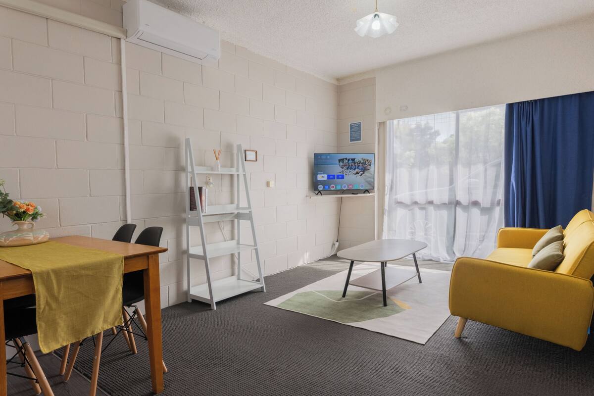 Una habitación con una mesa de comedor, sillas, un sofá, un televisor y una ventana con cortinas.