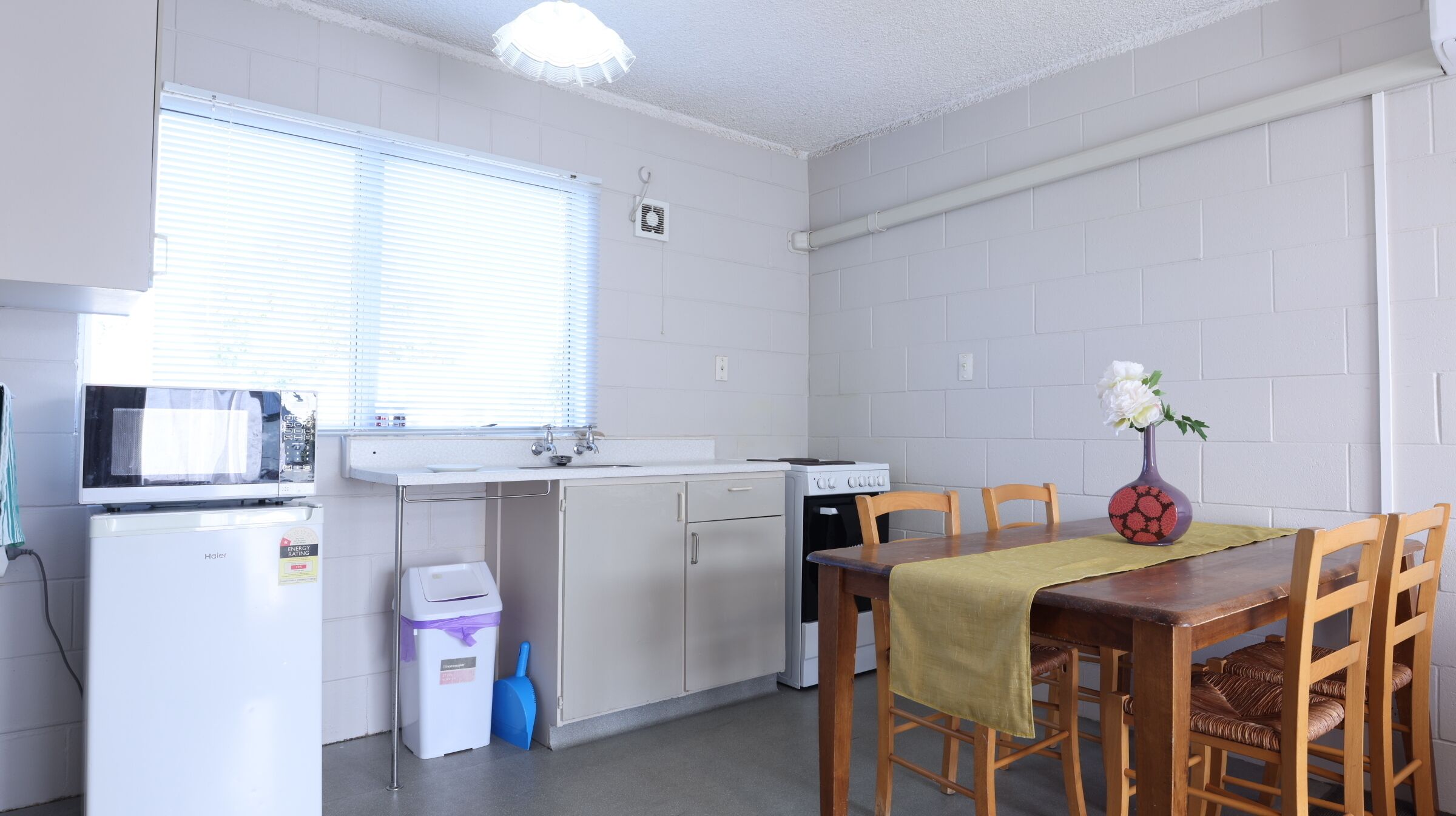 A compact kitchen with a microwave, stove, and sink. There is a dining table with chairs and a vase with flowers.