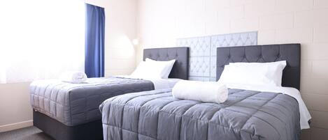 Habitación de hotel con dos camas, una ventana con cortinas azules y una pared de ladrillo blanco.