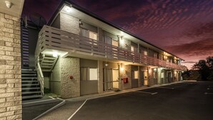 A motel with a staircase leading to a second floor, a parking lot, and a sunset sky. - Claudelands Motel (Hamilton)