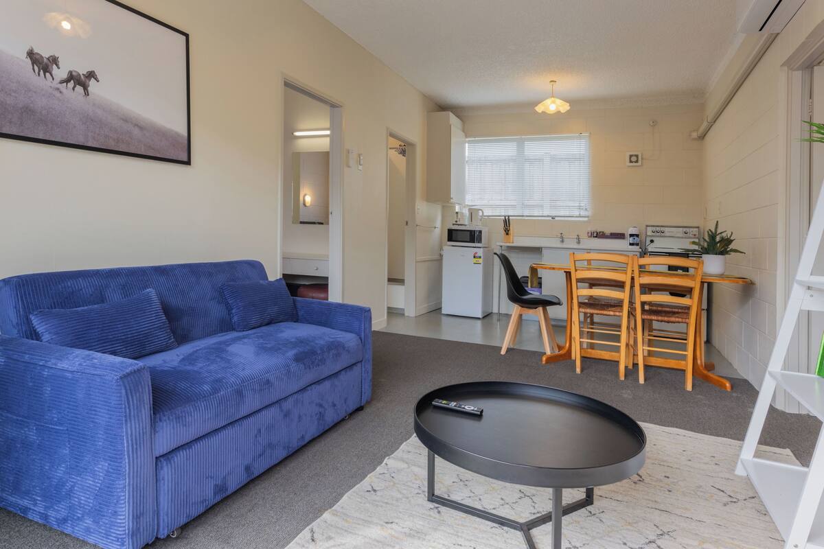 Una sala de estar con un sofá azul, una mesa de centro y una zona de cocina con una mesa de comedor y sillas.