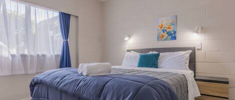 A bedroom with a bed, a nightstand, a painting on the wall, and a window with curtains.