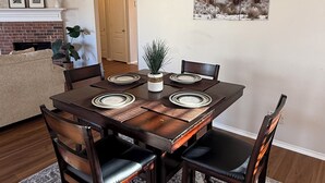 A dining room with a rectangular table, six chairs, a chandelier, a fireplace, and a framed picture on the wall.