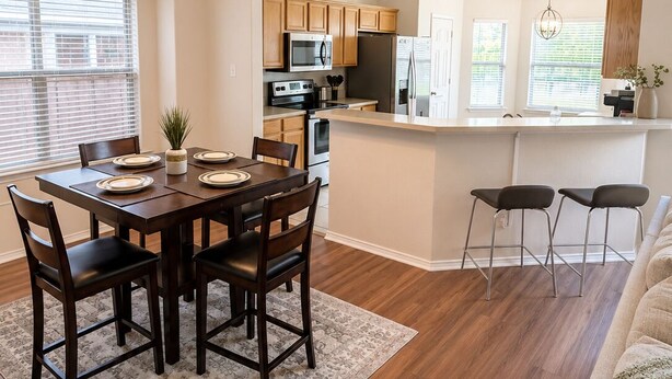 A modern kitchen with wooden cabinets, a central island, and a dining area with a table and chairs.