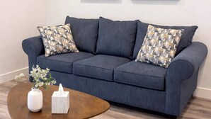 A blue sofa with patterned cushions, a wooden coffee table with a vase and tissue box, and abstract paintings on the wall. - Resort 1BR Oasis Pool Spa Gym Reno Getaway (Reno)