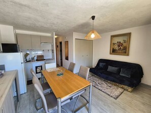 A compact living space with a dining table, chairs, a sofa, a kitchen area, and a hanging light fixture. - Studio, sea view, WIFI, A/C, all on foot (ST MANDRIER SUR MER)