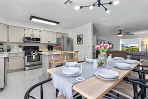 A modern kitchen with white cabinets, stainless steel appliances, and a dining area with a table set for four. - Luxury 4BR Retreat with Pool, Arcade, and Games (Henderson)