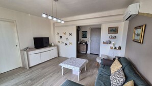 Een woonkamer met een bank, een salontafel, een televisie en een eethoek met een kast en een stoel.