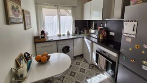 Een functionele keuken met een wasmachine, een koelkast en een eethoek met een tafel.