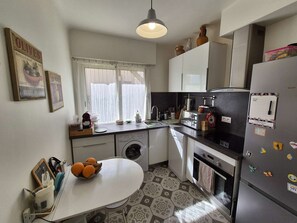 A compact kitchen with a washing machine, a refrigerator, and a dining area with a table. - 2 rooms, WIFI, A/C, heart of les Sablettes (LA SEYNE SUR MER)