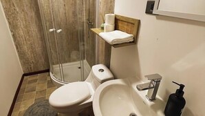 Un baño con ducha, inodoro, lavamanos y un perchero para toallas.