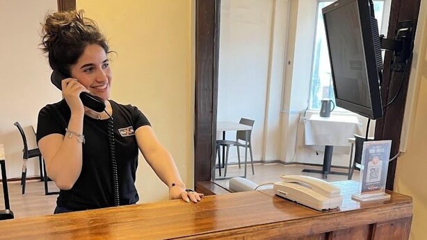 Un mostrador de recepción con detalles de madera, un teléfono y un televisor montado en la pared.