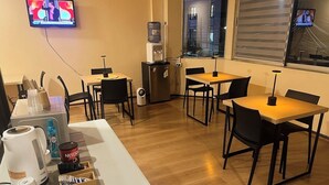 Habitación de hotel con kitchenette, televisor montado en la pared, dispensador de agua y ventana con vistas.