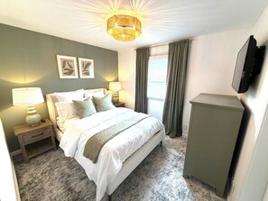 A bedroom with a bed, bedside lamps, a television, and a window with curtains.