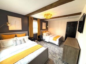 A hotel room with two beds, a wooden ceiling, a chandelier, and a television.