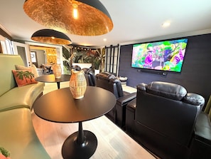 A modern living room with a sofa, a dining table, a TV mounted on the wall, and a decorative vase.