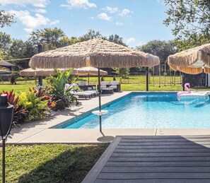 A swimming pool with thatched umbrellas, lounge chairs, and a flamingo float.
