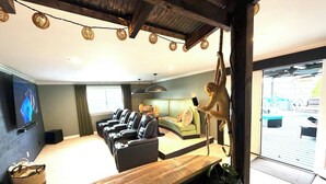 A modern living room with a sofa, a wooden coffee table, and a television. - Barefoot Tiki Retreat -Inground Heated Pool, Hot Tub, Game Rm,Theater Rm,Firepit (Mason)