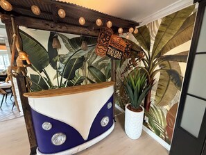 A room with a blue and white boat-shaped counter, a sign reading 'The Barefoot Bar,' and a large tropical plant.