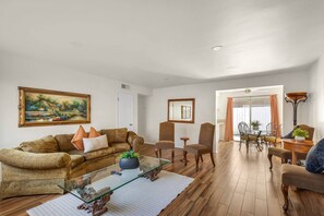 A living room with a sofa, chairs, a glass coffee table, and a dining area with a table and chairs. - 2bd/2bth Nobel Delight, Close To South Coast Plaza (Santa Ana)