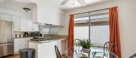 A modern kitchen with white cabinets, a stainless steel refrigerator, and a dining area with a glass table and chairs.