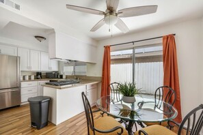 A modern kitchen with white cabinets, a stainless steel refrigerator, and a dining area with a glass table and chairs. - 2bd/2bth Nobel Delight, Close To South Coast Plaza (Santa Ana)