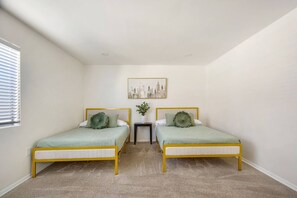 A bedroom with two beds, a small table, a plant, and a cityscape painting on the wall. - 2bd/2bth Nobel Delight, Close To South Coast Plaza (Santa Ana)