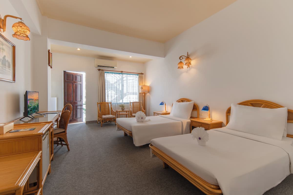 A hotel room with two beds, a desk, a chair, a lamp, and a window.