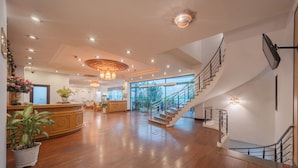 A spacious lobby with a wooden floor, a reception desk, a staircase, and a large window. - Green Hotel Nha Trang (Nha Trang)