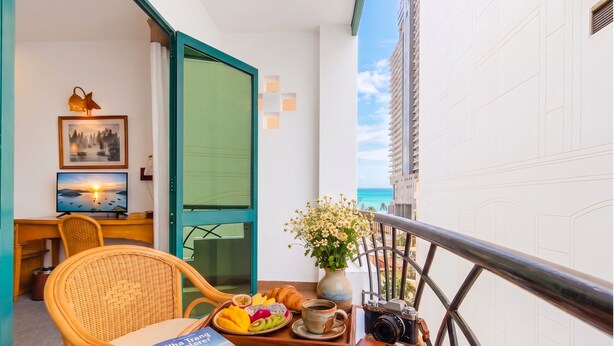A balcony with a dining table, a wicker chair, a book, a camera, and a vase with flowers. - Green Hotel Nha Trang (Nha Trang)