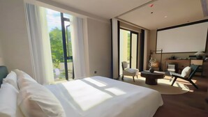 A modern hotel room with a large bed, a seating area with a chair and table, and a balcony with a view of greenery. - Quanzhou About Meisu (Quanzhou)