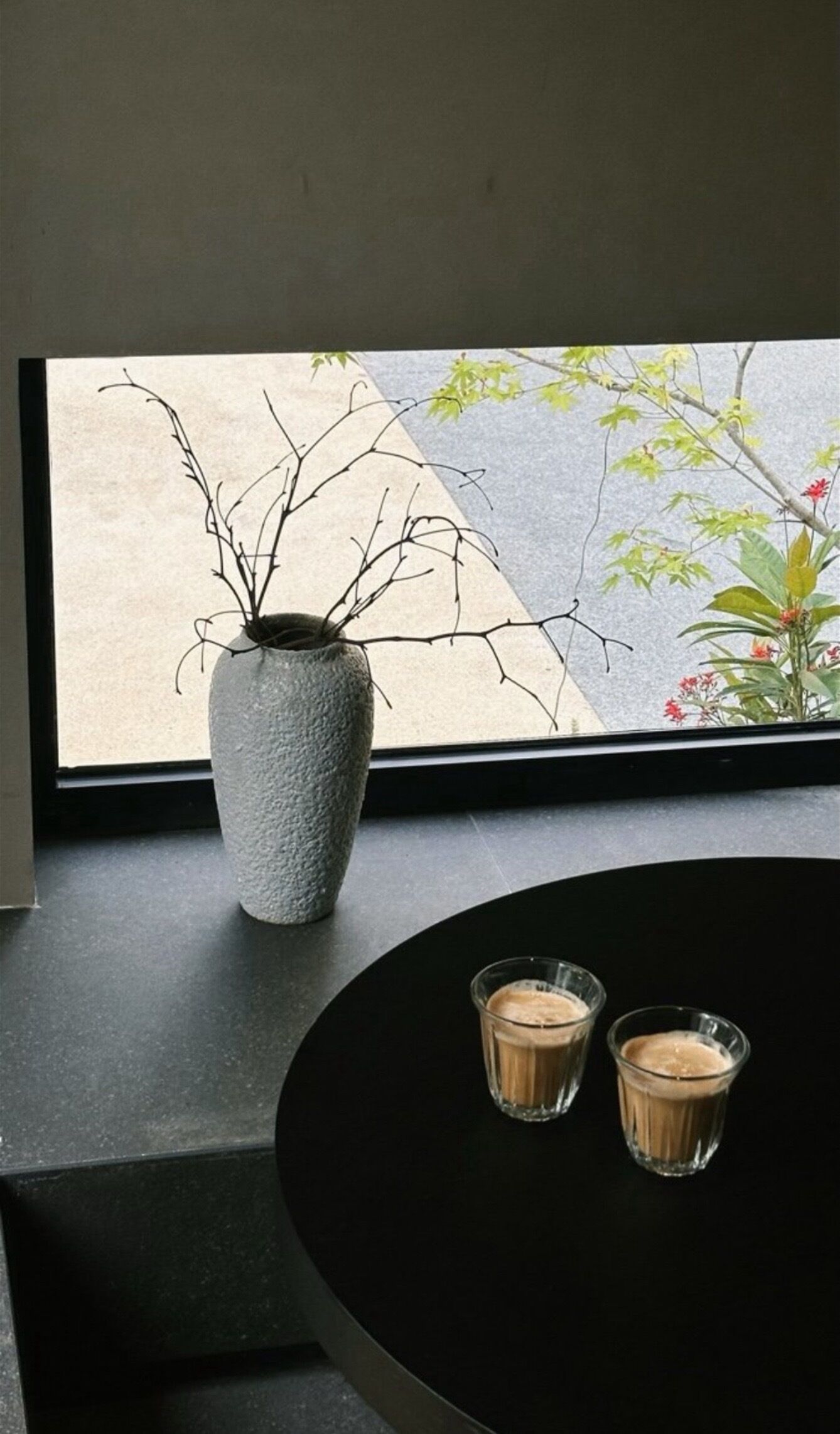 Una ventana con vista a un árbol y un jarrón con ramas en el alféizar.