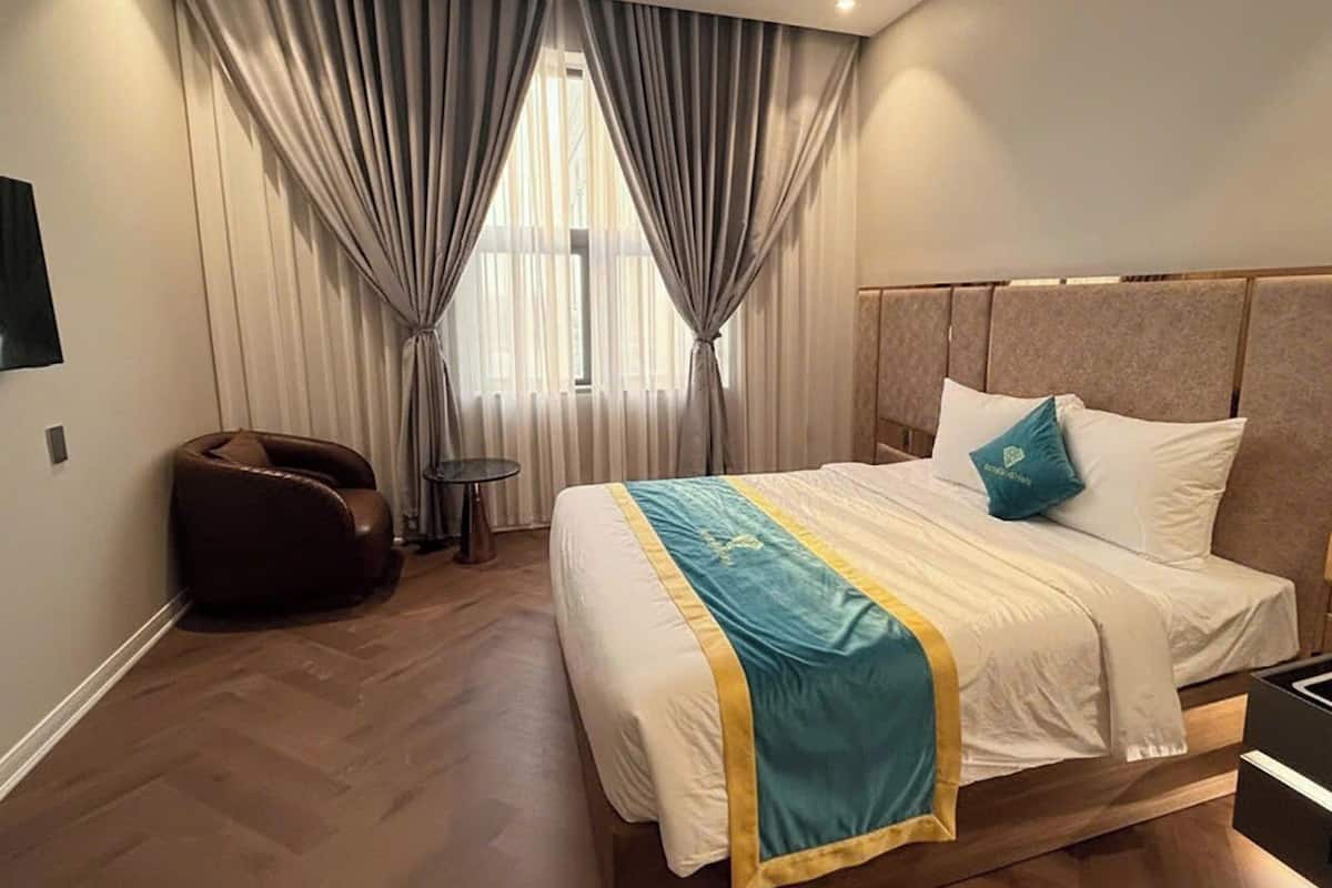 A modern hotel room with a large bed, a headboard, a small side table, and a leather chair.