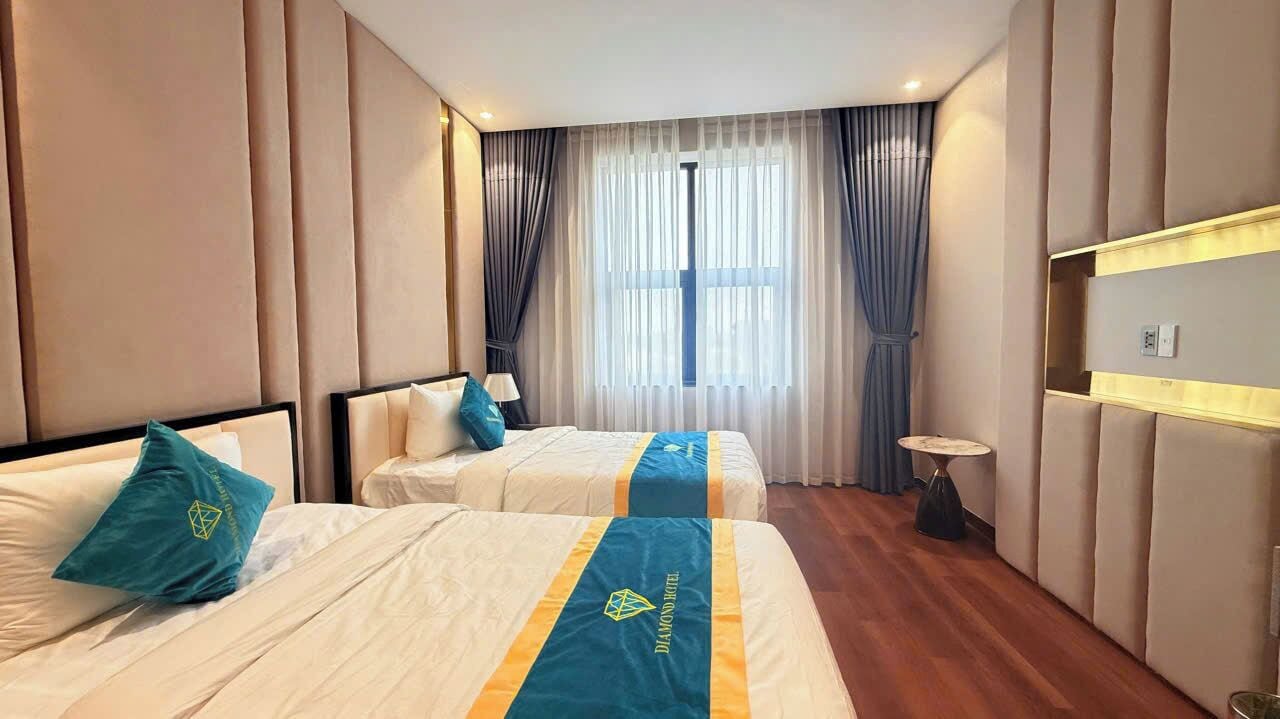 A hotel room with two beds, a small table, and a large window with curtains.