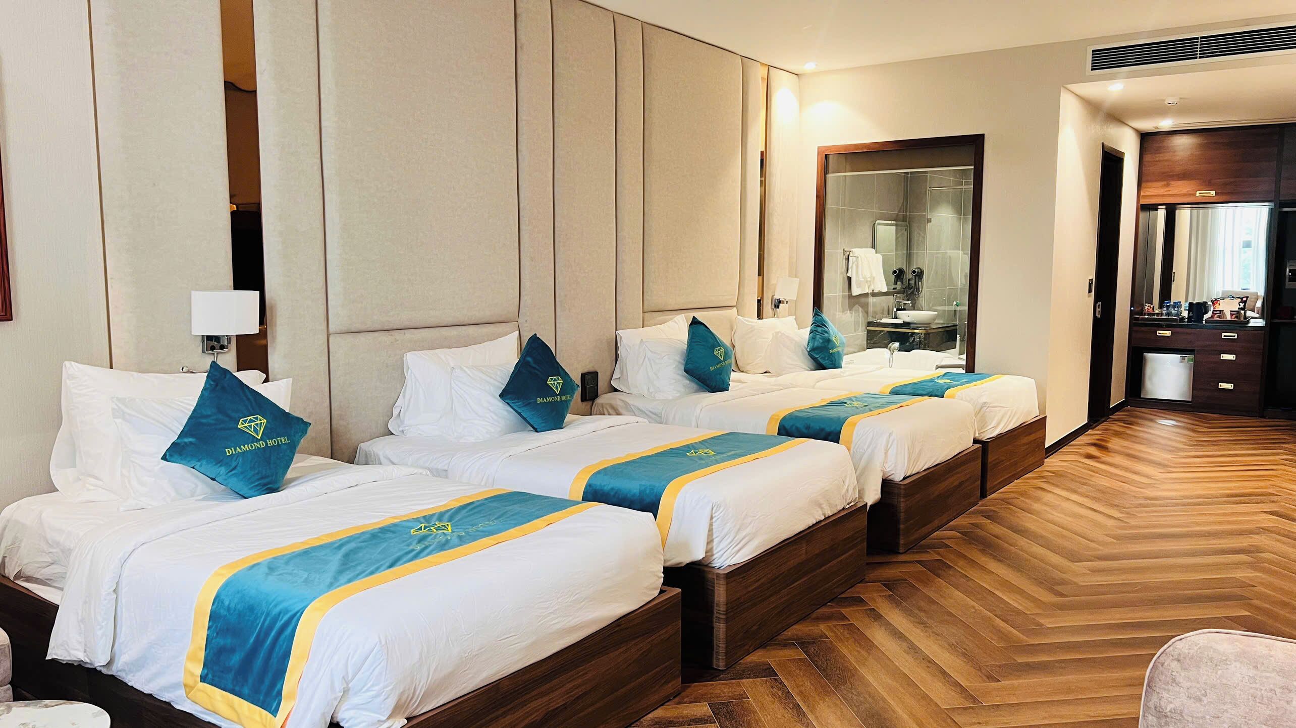 A hotel room with four beds, each with a blue and yellow bedspread, and a wooden herringbone floor.