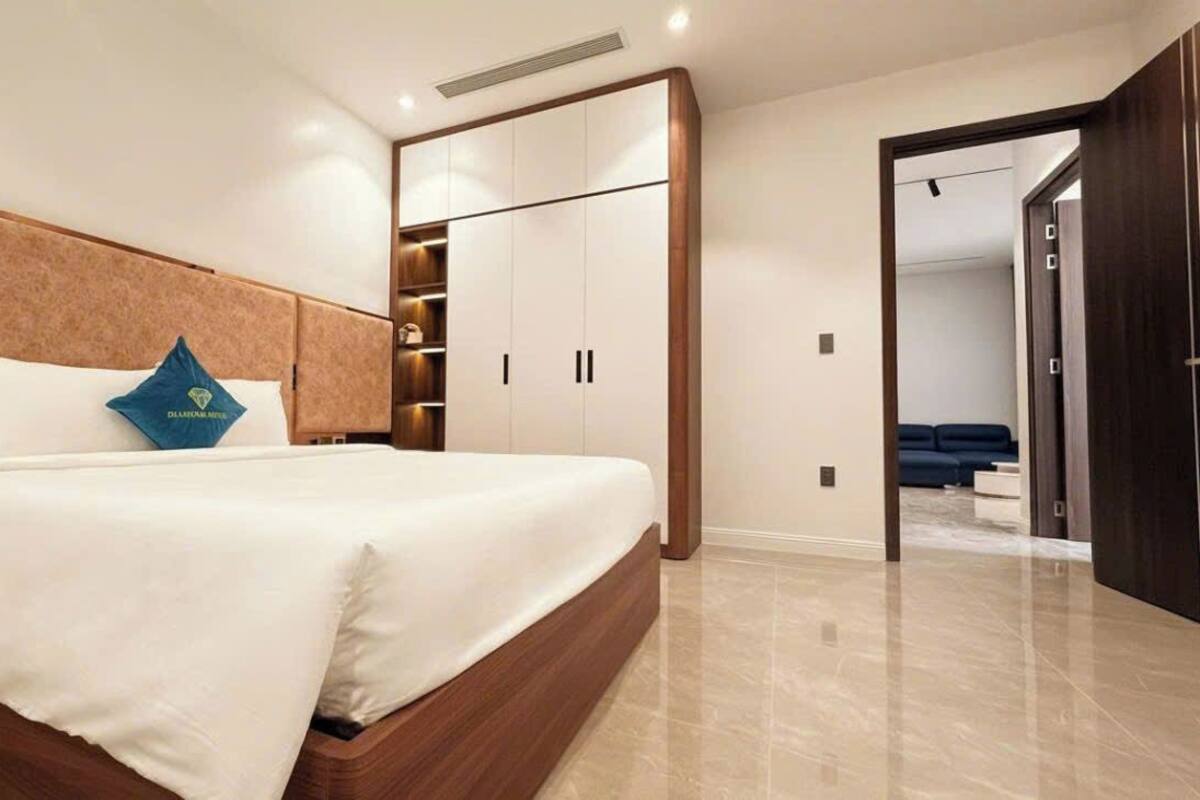 A modern bedroom with a large bed, built-in wardrobe, and a view into another room.