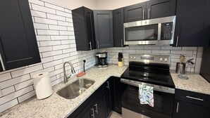 A modern kitchen with black cabinets, a stainless steel microwave, a stove, and a granite countertop. - Downtown Jim Thorpe Stay at Charles Albright (Jim Thorpe)