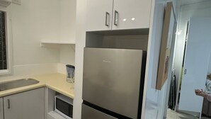 Eine moderne Küche mit einem Edelstahlkühlschrank, weißen Schränken, einer beige farbenen Arbeitsplatte und einem Fenster.
