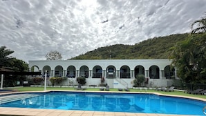 Ein Pool mit einer Fliesenverkleidung, ein Gebäude mit Rundbogenfenstern und eine grüne Rasenfläche.