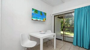 Ein Zimmer mit einem weißen Tisch und Stühlen, einem Bild mit einer Strandansicht und einer Schiebetür zu einem Außenbereich.